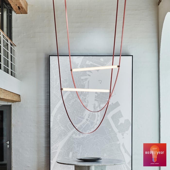 A pair of intersecting WireLine suspension light fixtures, designed for Flos by design studio Formafantasma, hang over a table in an open studio space. The Interior Design Best of Year badge appears in the lower right corner.