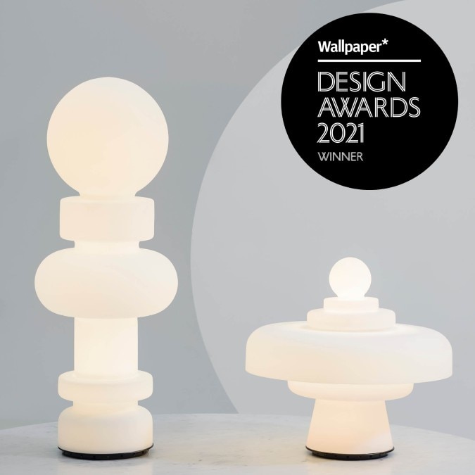 A studio image of FontanaArte's 2021 reissue versions of lighting designer Bobo Piccoli's Re table light and Regina table lamp, side-by-side and illuminated. The Wallpaper* Design Award badge appears in the upper right corner.