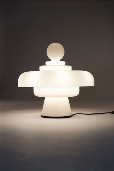 A moody photo of Bobo Piccoli's Regina table light for FontanaArte casting its light in a darkened space.