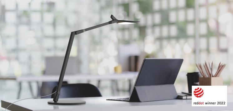 Splitty Reach table light extends over a laptop, providing task lighting. The Red Dot Design Award badge appears in the lower right corner.