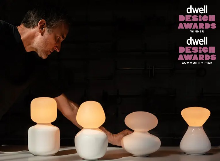 Lighting designer David Weeks leans over his Reflection collection of lights: Oblo table light, Enno table light, Oval table light, and Noma table light. Dwell Best Lighting and Dwell Community Pick badges appear in the upper right corner.