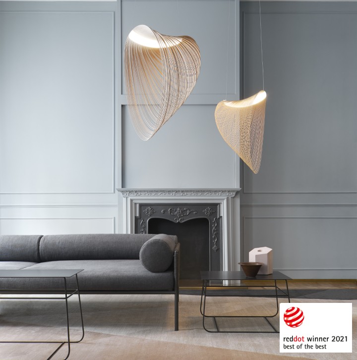 A pair of Illan suspension lights, one large one small, designed for Luceplan by Zsuzsanna Horvath, hang above a sparing minimalist living room. The Red Dot Best of the Best badge appears in the lower right corner.