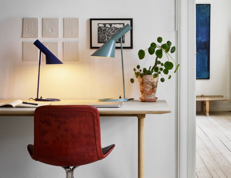 AJ Mini table lamp in blue and AJ desk light in pale petroleum finish sit upon a wooden work surface in a sparsely-decorated modern home office.