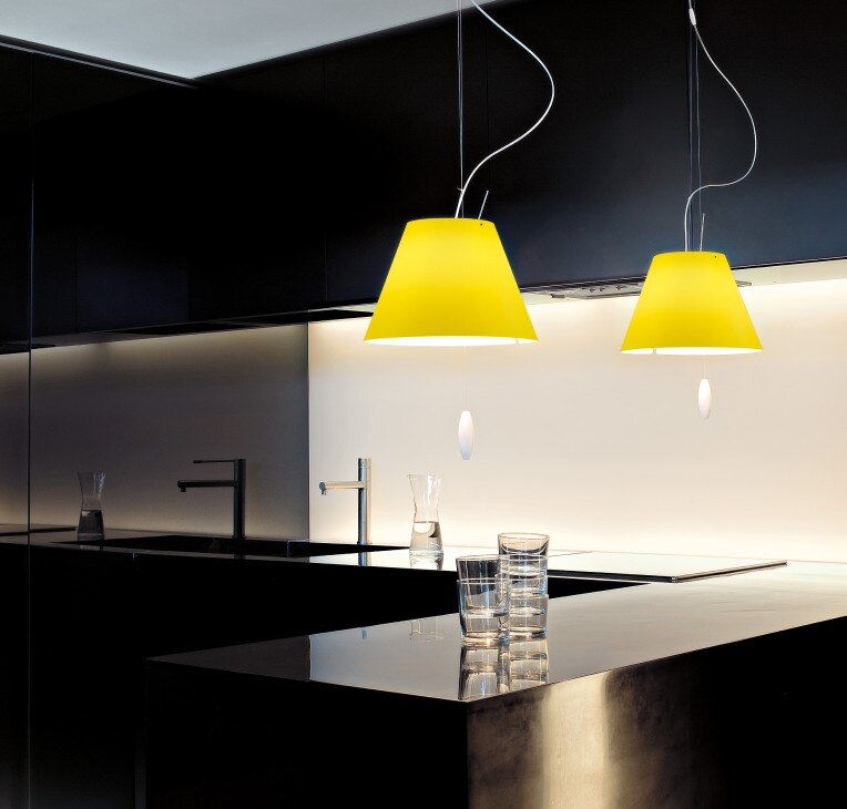 A pair of bright yellow Costanzina pendant lights, designed by Paolo Rizzatto for Luceplan, add colour and vivacity to a contemporary black-and-white kitchen 