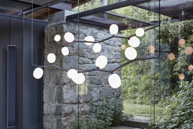 An glass-walled corridor between two buildings with Lucie Koldova's Ivy Horizontal linear suspension lights hanging inside.