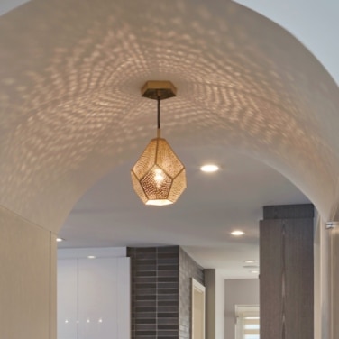 An arched hall leading to a bright modern kitchen bears an intricate pattern of light and shadow from Dounia Home's Almas pendant light.