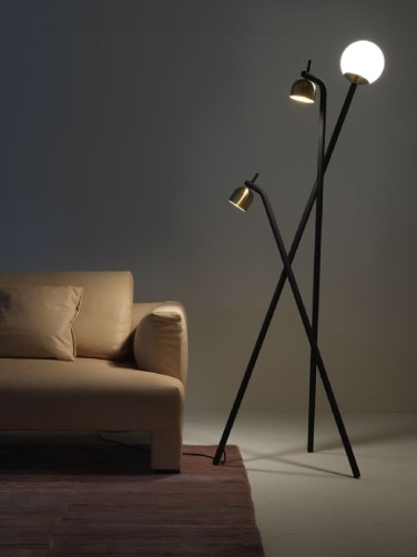 FontanaArte's Tripod floor light by Front Design stands on a studio set next to a plush sofa.