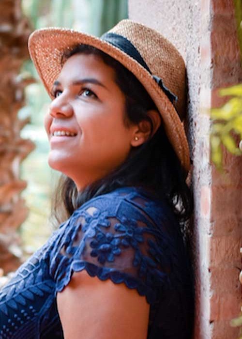 Dounia Tamri-Loeper leans against an exterior wall, smiling as the sun strikes her Panama hat.