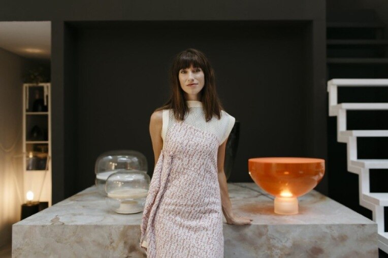 Lucie Koldova stands in front of a marble table, on which sits her own Macaron and Lightline designer lights