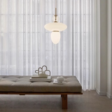 Rizzatto 43 pendant light, designed by Paolo Rizzatto for Nuura, hangs above a plush upholstered bench before a bank of windows in a luxurious bedroom.