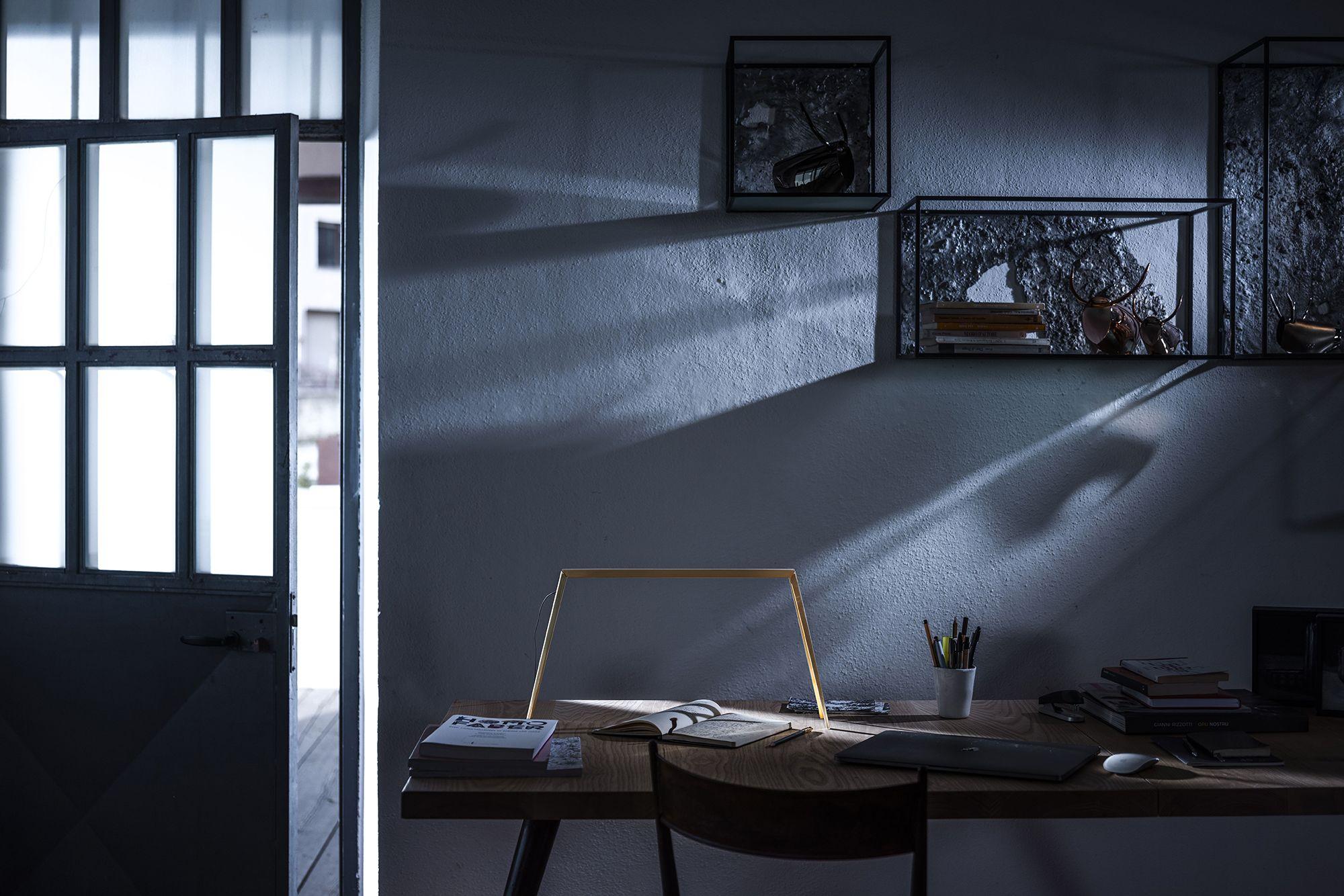 The Bridge table lamp in brass, placed on top of a desk